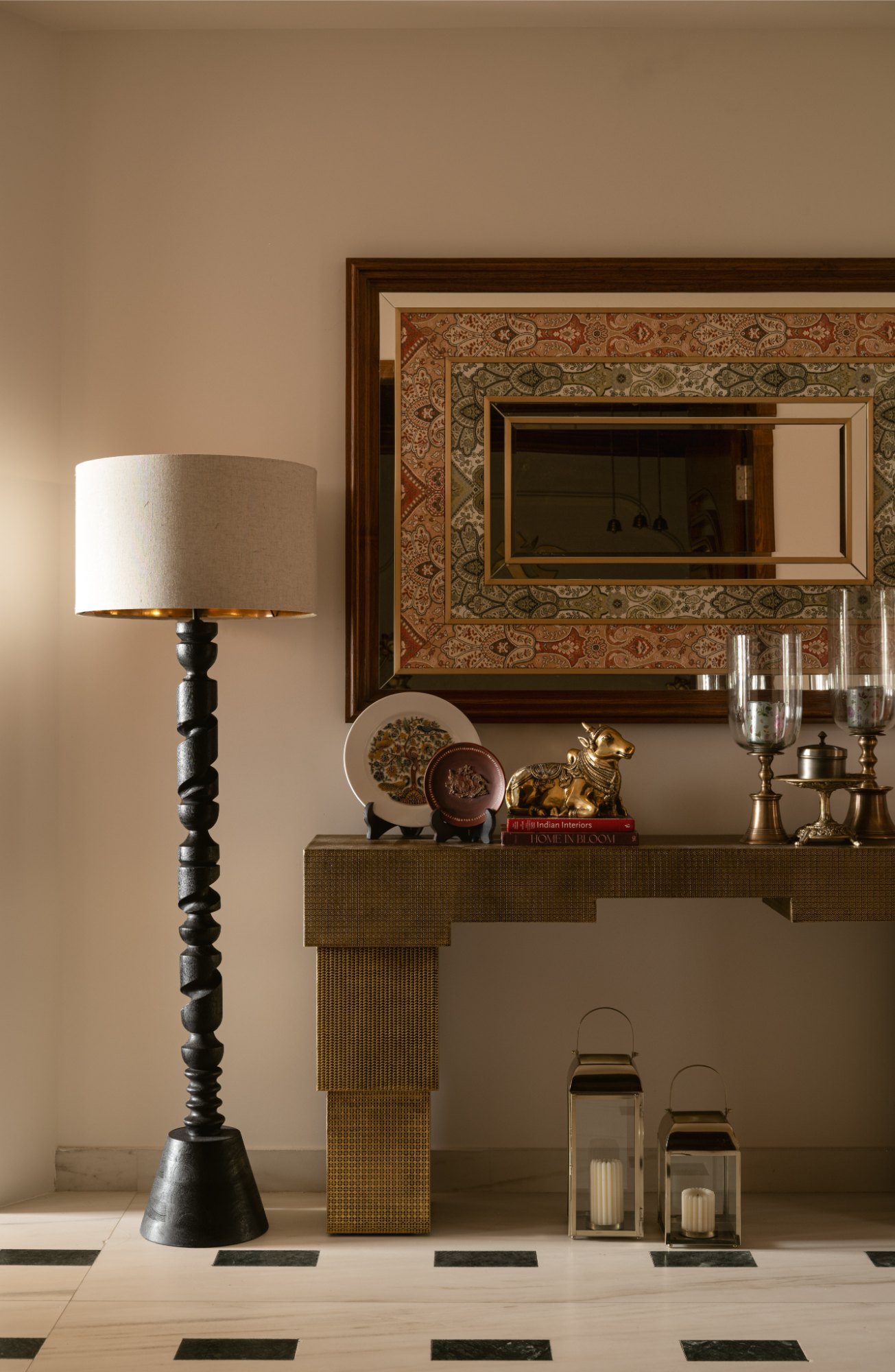 Foyer console in cane texture beneath a paisley-framed mirror with brass objects