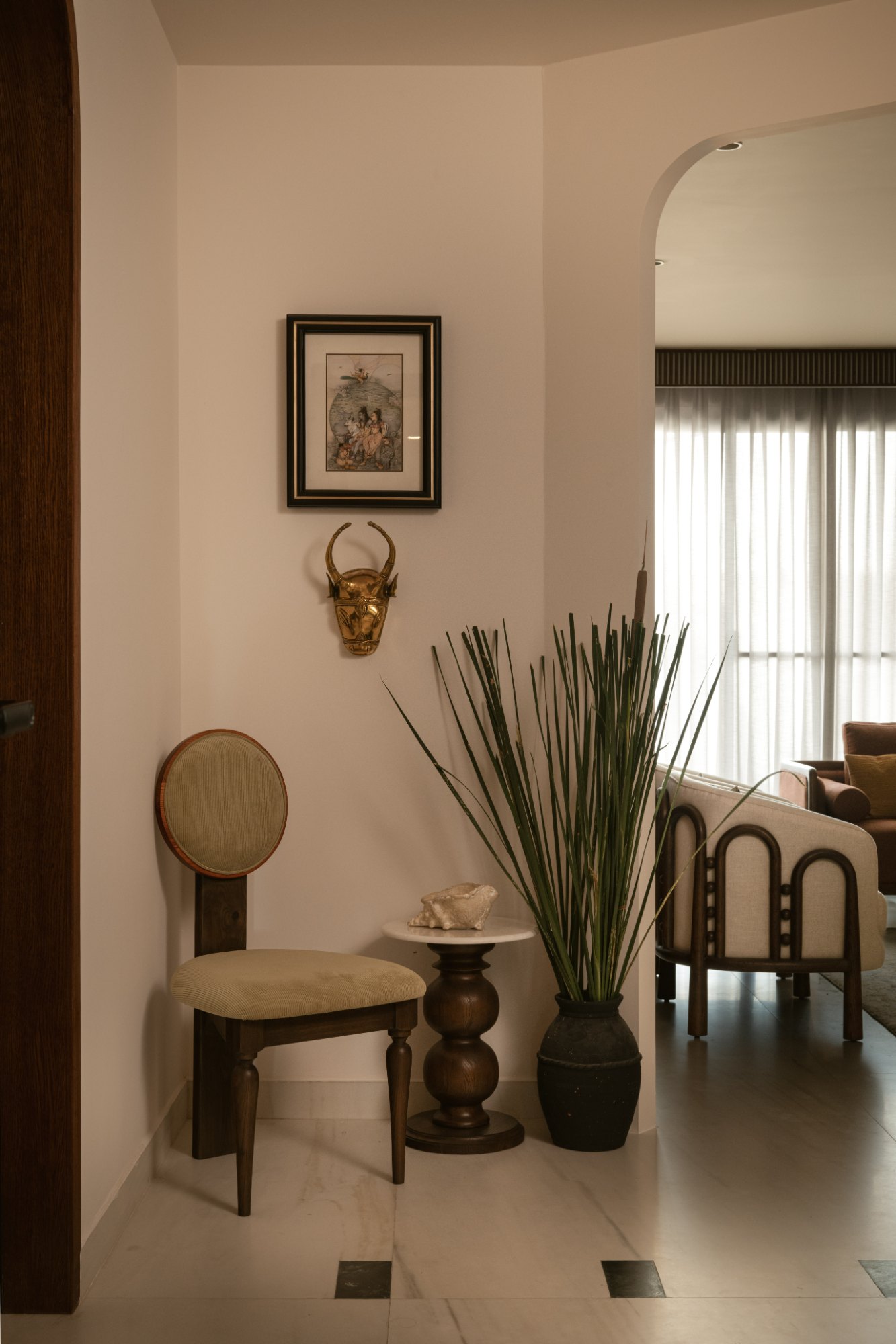 Foyer corner with a round-back chair, brass nandi mask and reeds in a black urn