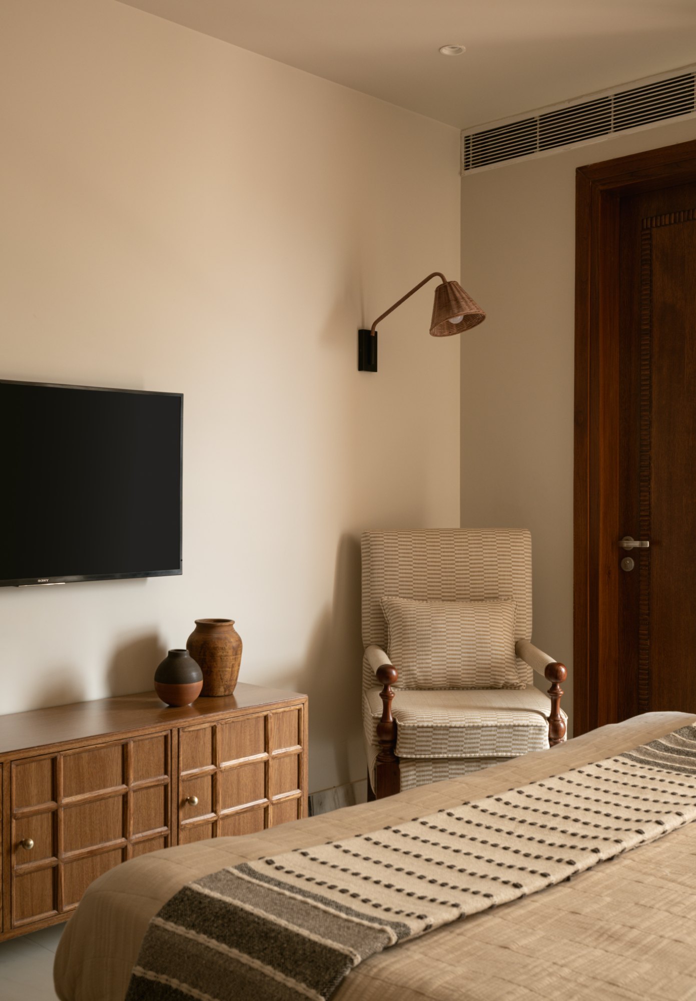 Bedroom seating corner with checkered upholstered chair and rattan wall light