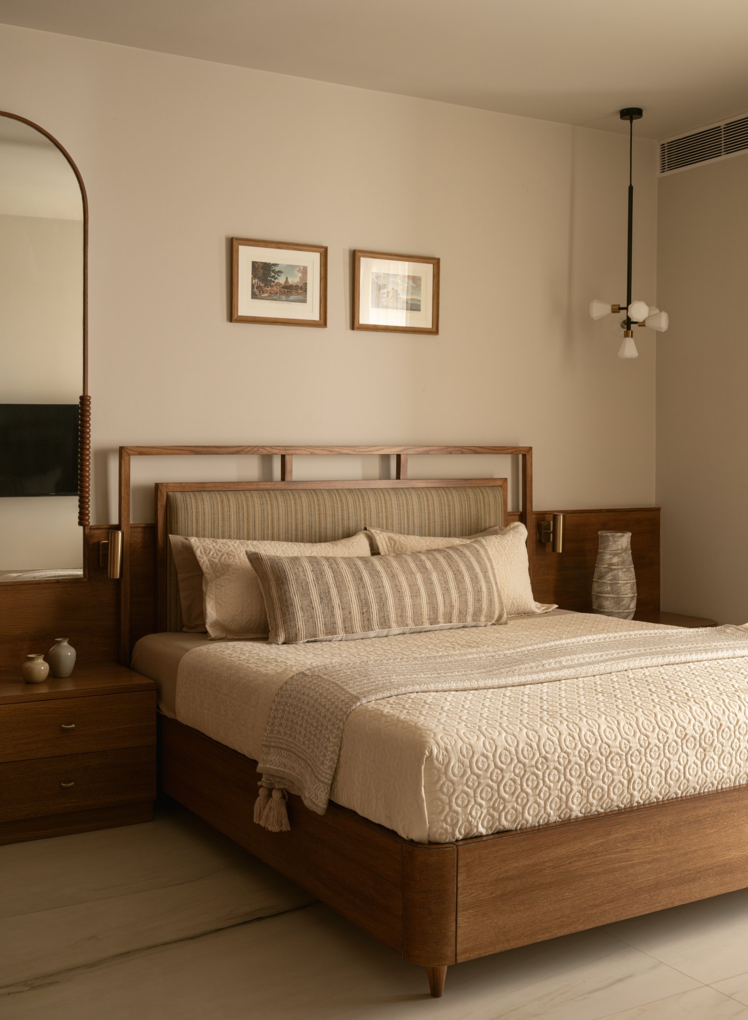 Bed with striped upholstered headboard, brass reading lights and framed prints