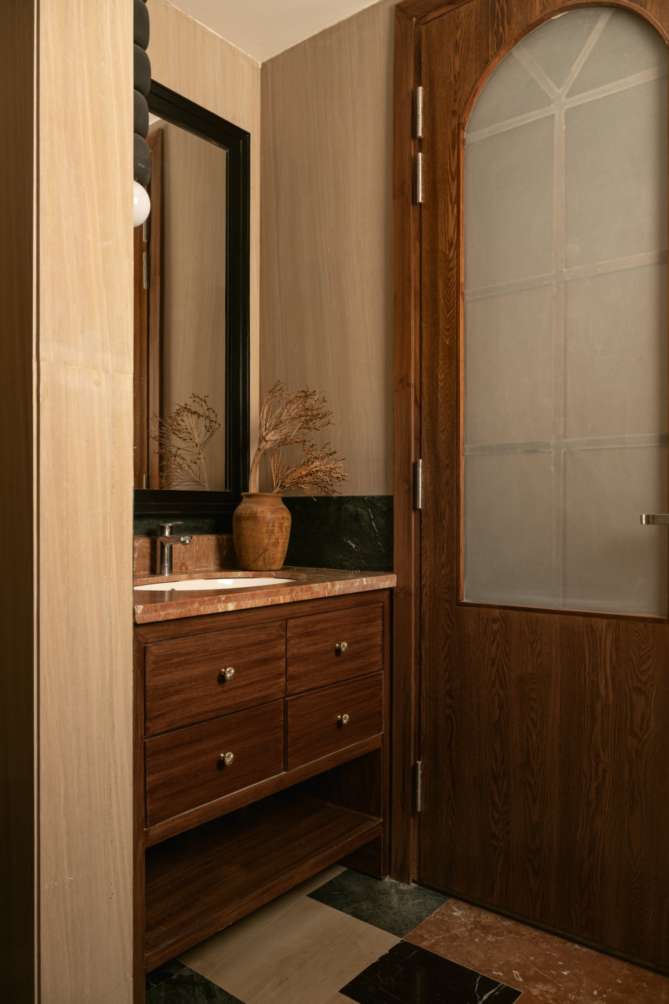 Bathroom vanity in dark wood with red stone counter and arched frosted door
