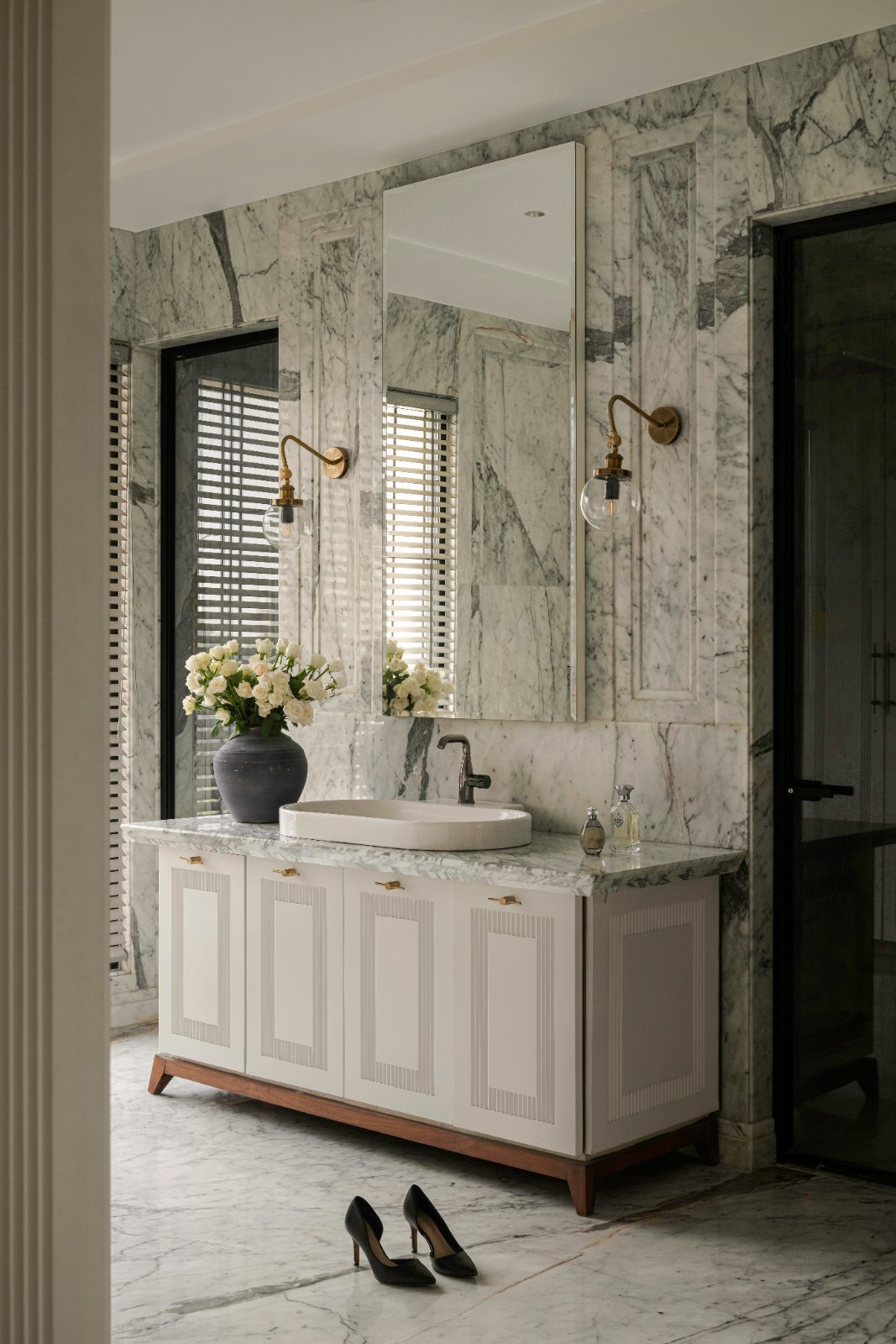 Marble bathroom with book-matched stone, brass sconces and a fluted vanity