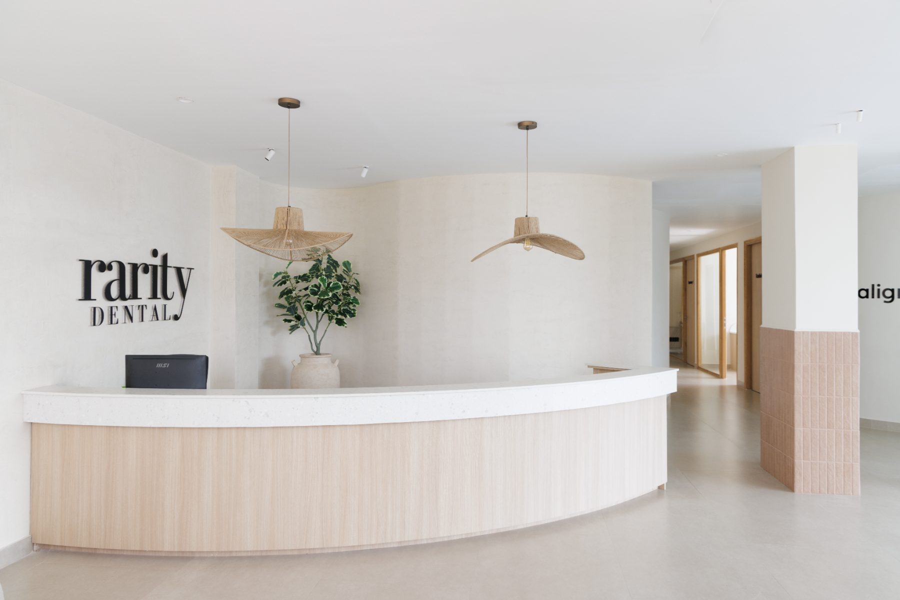 Rarity Dental reception — curved oak desk, plaster wall and woven pendants