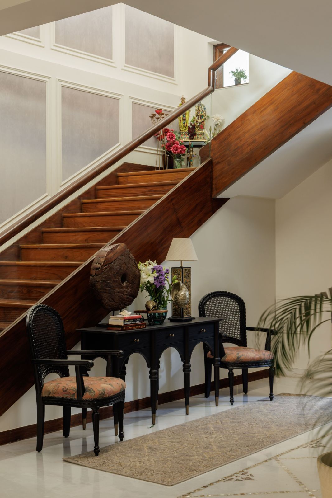 Teak staircase with a black arched console and cane chairs