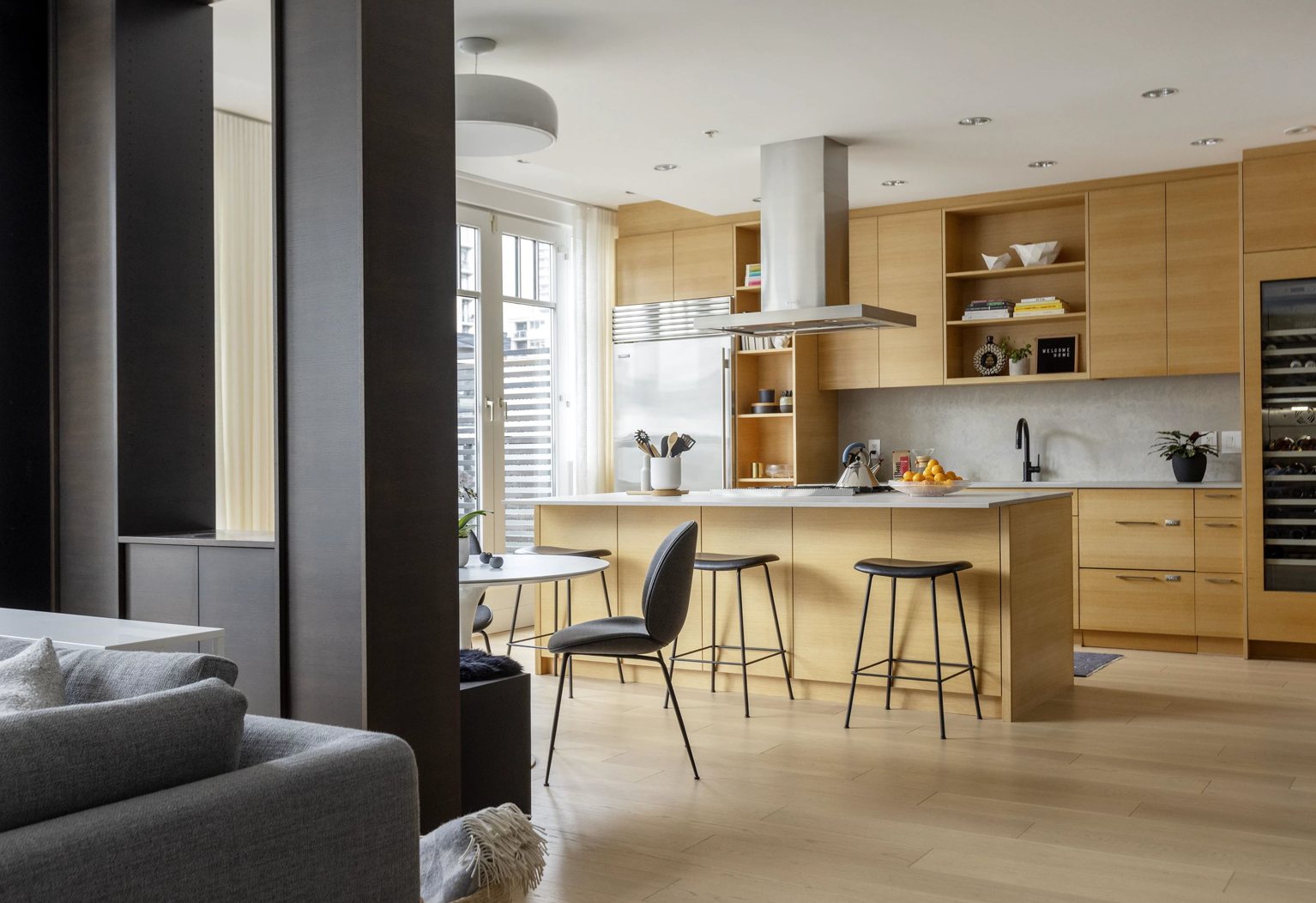 Oak kitchen island with stainless hood, black stools and warehouse windows